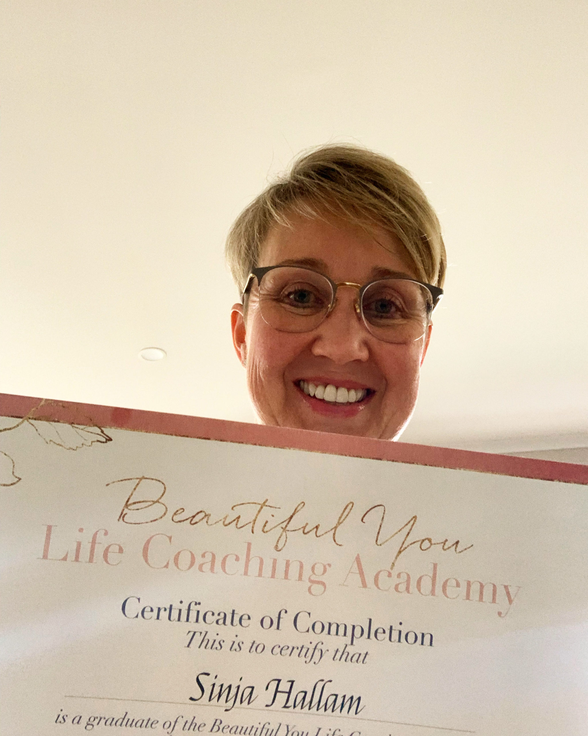 Sinja facing into the camera holding her BYCA Life Coach Certificate