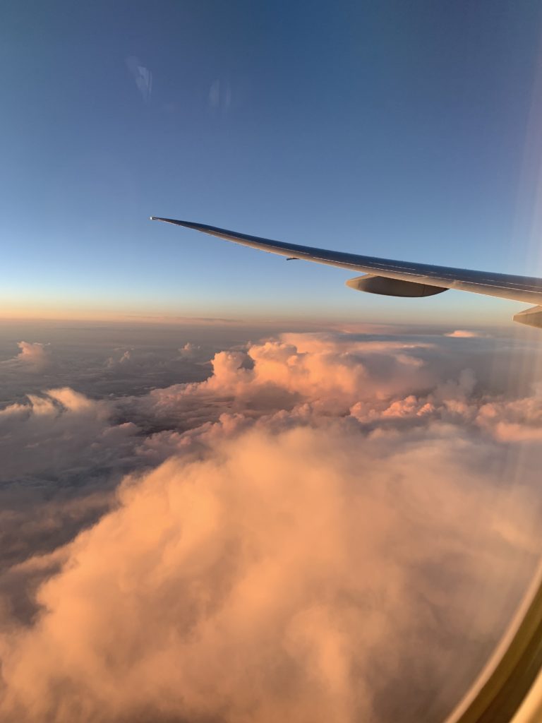 Viewing clouds, a sunrise and a plane wing from inside a plane window. The sunrise represents the magic of new beginnings
