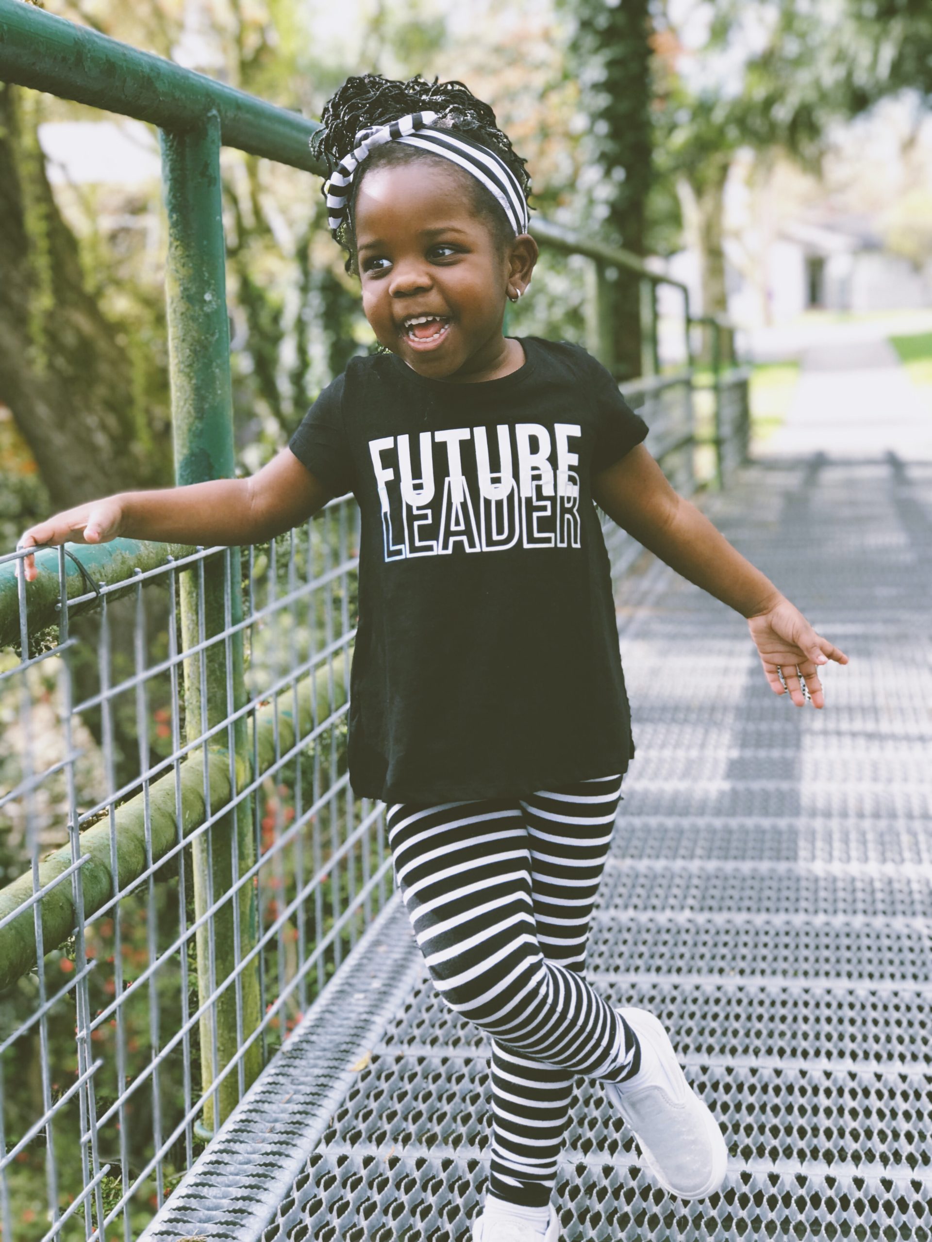 Little girl standing on bridge smiling & wearing a black t-shirt that reads Future Leader